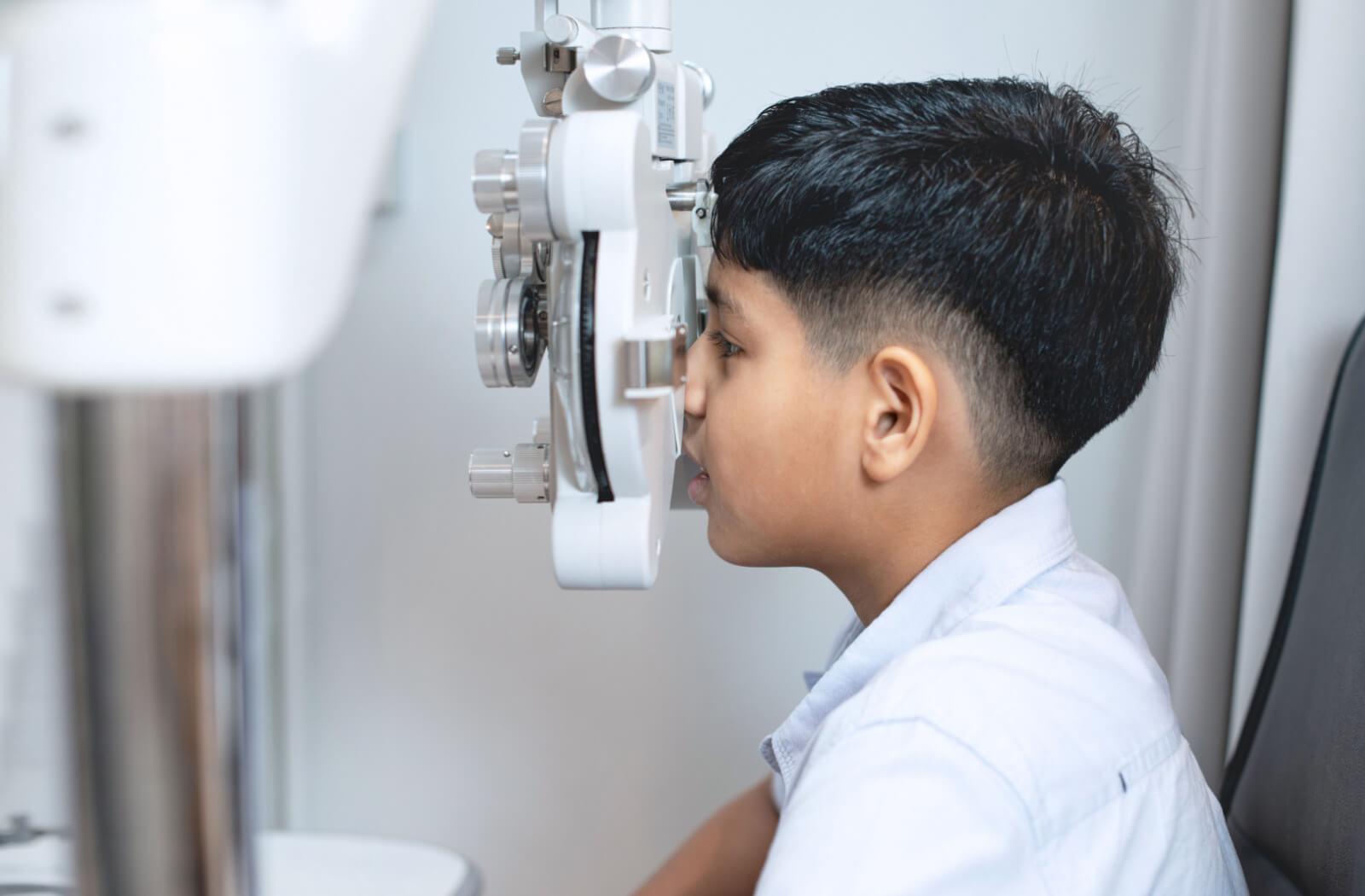 A child sitting in a vision therapist's office looking into a machine that tests his vision