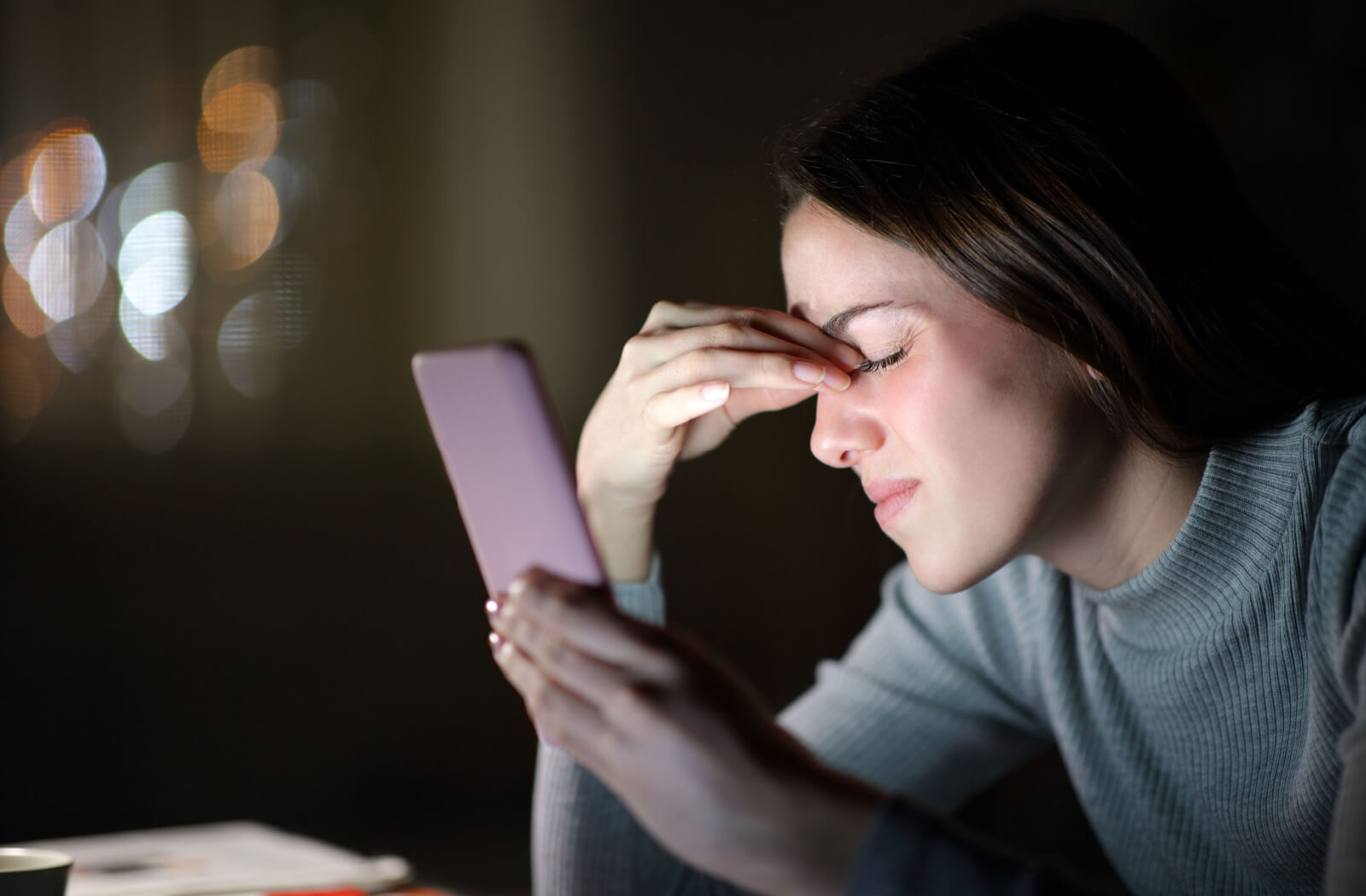 Tired woman suffering eyestrain using mobile phone in the night at home
