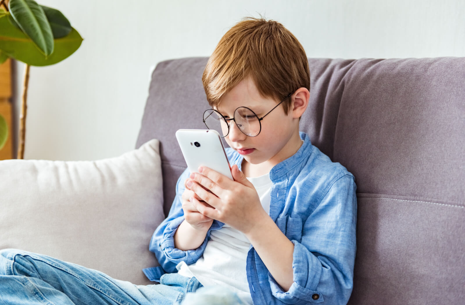 A small boy in glasses holding his smartphone close to his face to view the screen