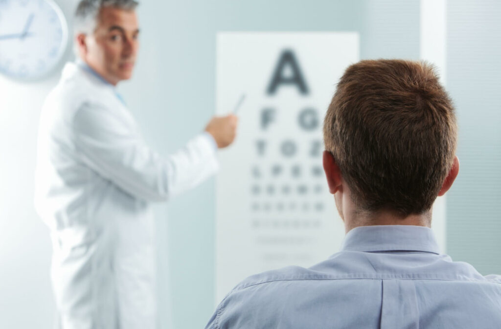 An eye care professional points to letters on a vision chart while a person sits facing the chart during an eye exam.