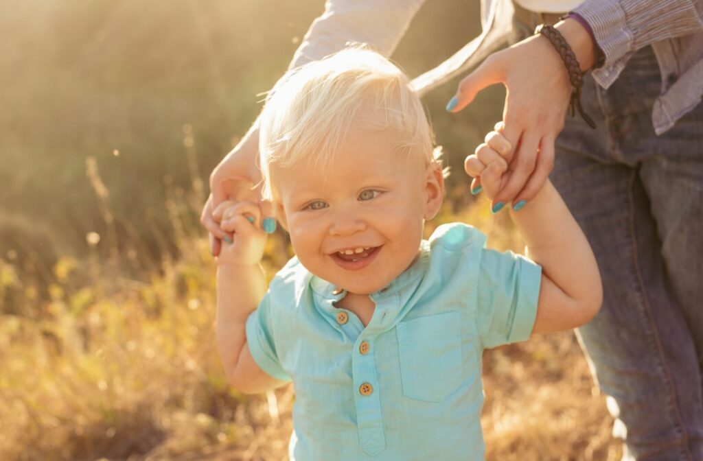 Crossed-eyed baby boy on nature in summer playing with mother on grass with sun rays on sunset