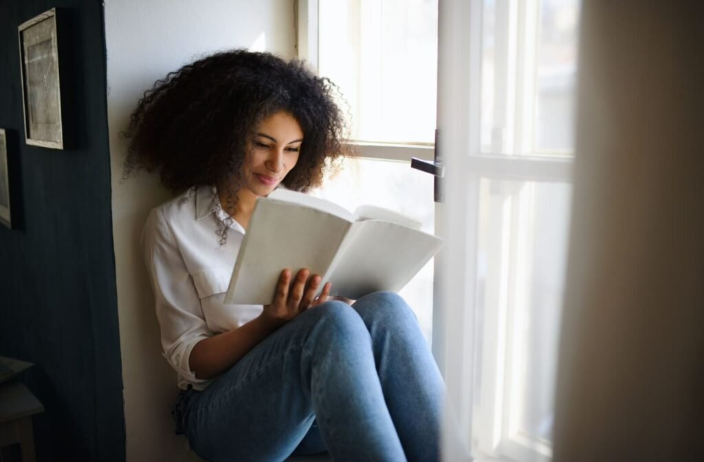 A young woman reading a book by the window to enhance her visual perceptual skills.