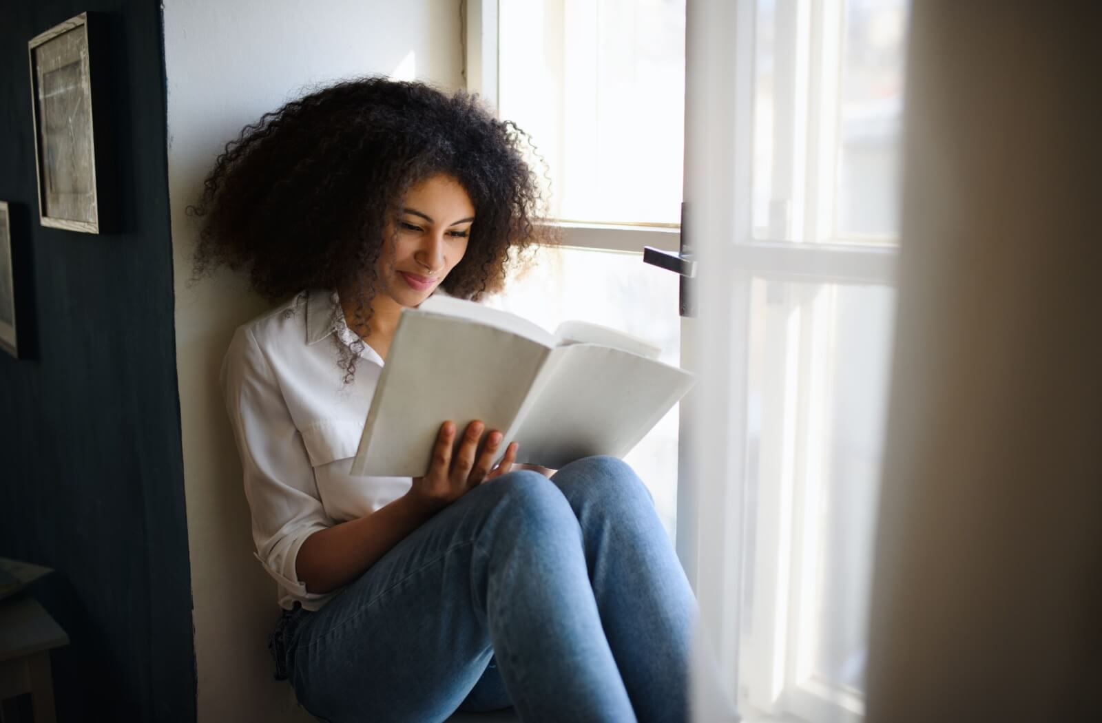 A young woman reading a book by the window to enhance her visual perceptual skills.