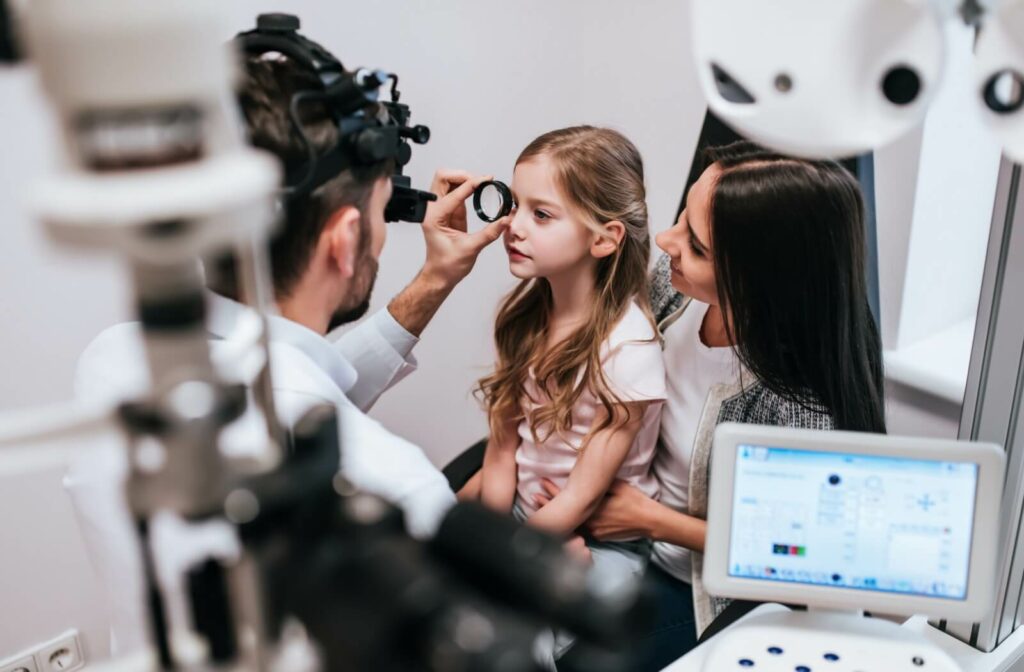 A young girl sitting on her mom's lap in a clinic has her vision examined by an optometrist