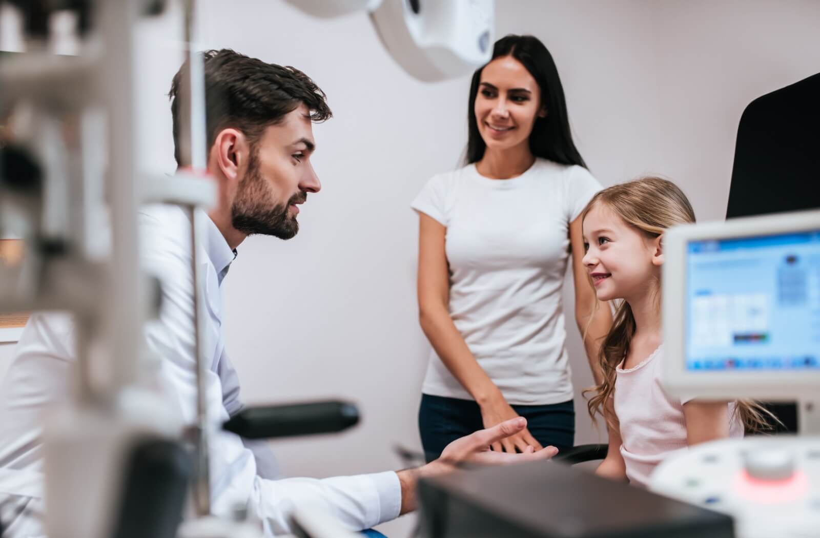 An eye doctor discussing vision therapy with a child and her mother during an eye exam.