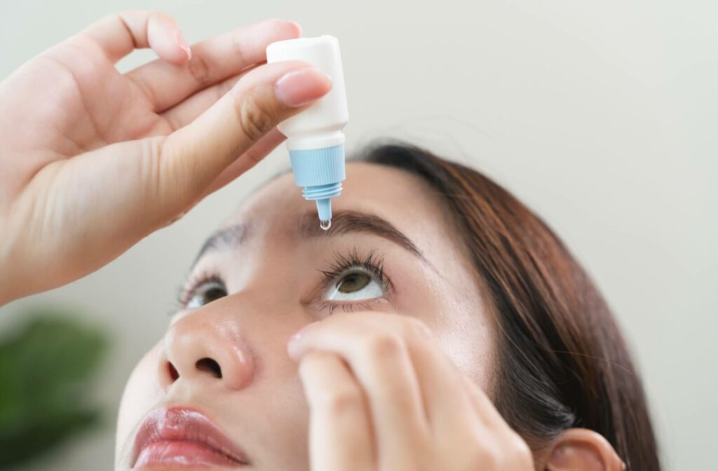 A person tilts their head back, preparing to apply eye drops to treat their dry eyes.