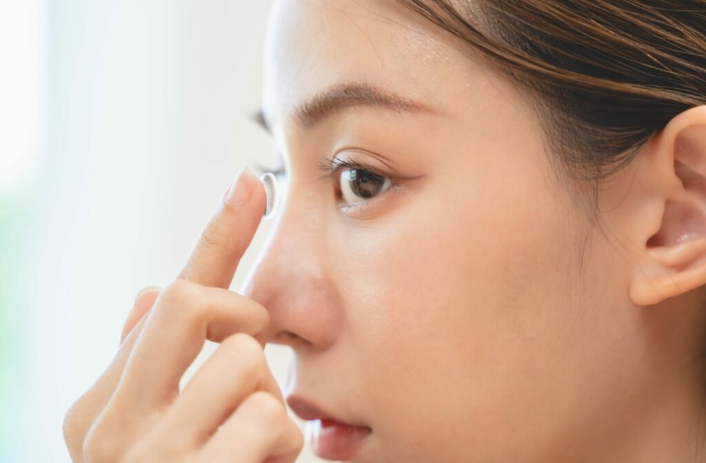 Close-up of a woman inserting a contact lens into her eye.