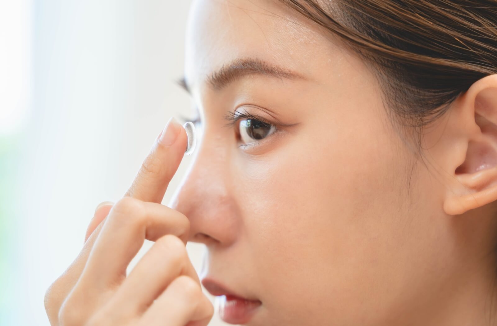 Close-up of a woman inserting a contact lens into her eye.