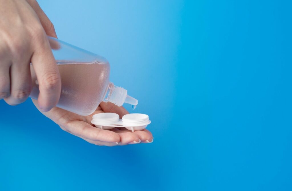 Person pouring contact lens solution into a contact lens case against a blue background.