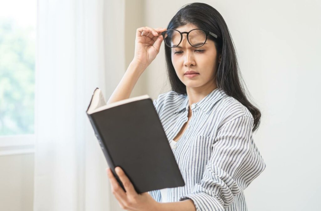 An individual lifting their glasses and squinting while trying to read a book.